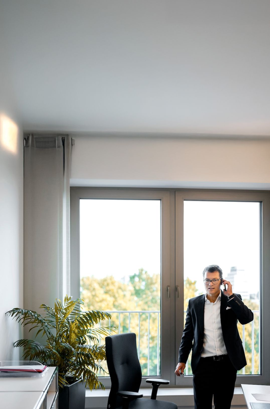 Ein COLLEGIUM Mitarbeiter steht telefonierend vor einem hellen Bürofenster